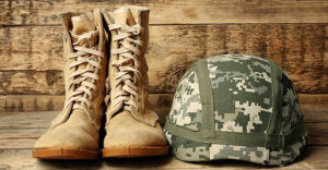 Pair of combat boots and military helmet on wooden background, close up